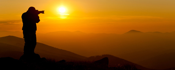 Pohľad na siluetu fotografa na vrcholkoch kopcov, ktorý fotí slovenskú krajinu pri západe slnka.